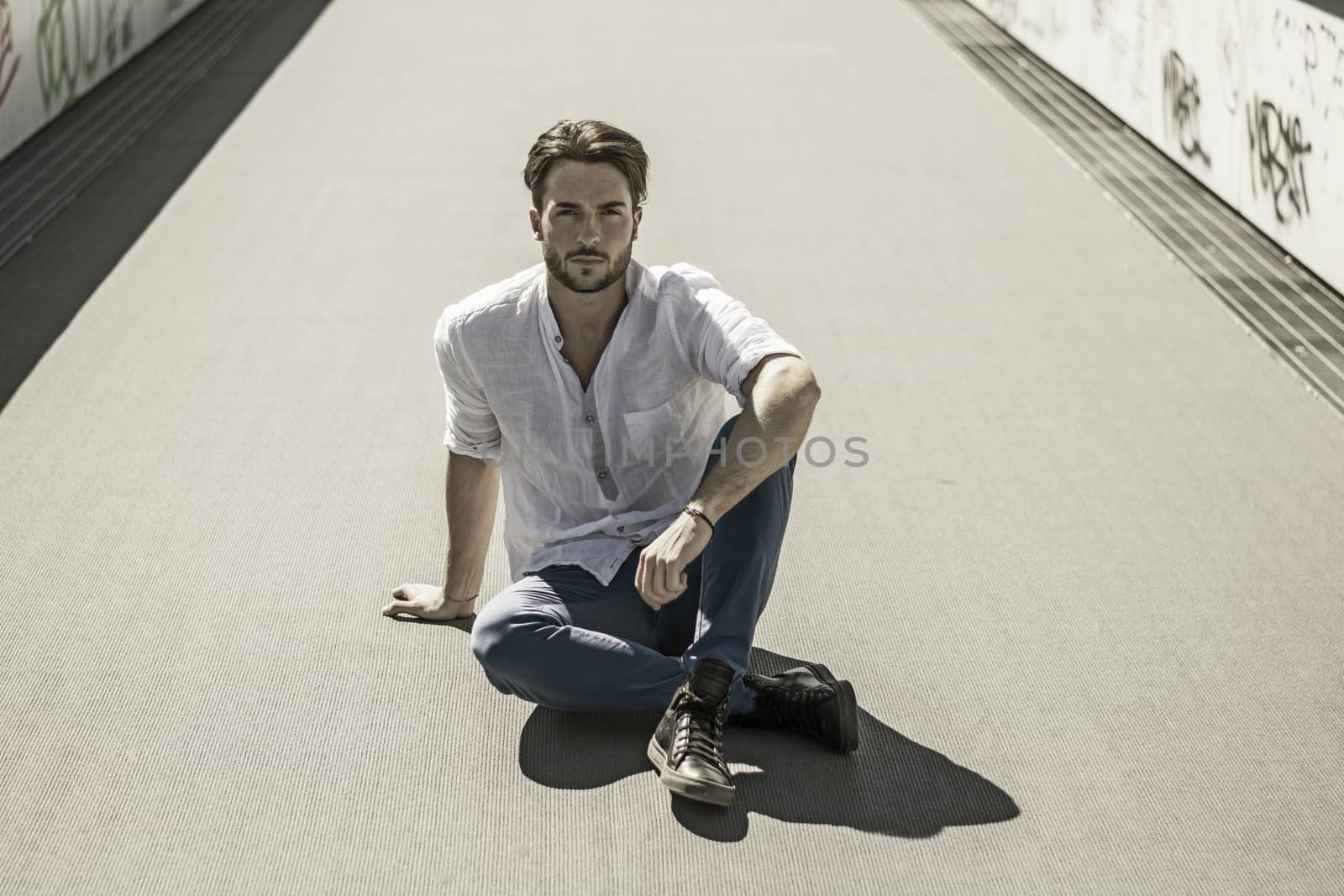 One handsome young man in urban setting in European city, sitting on the ground