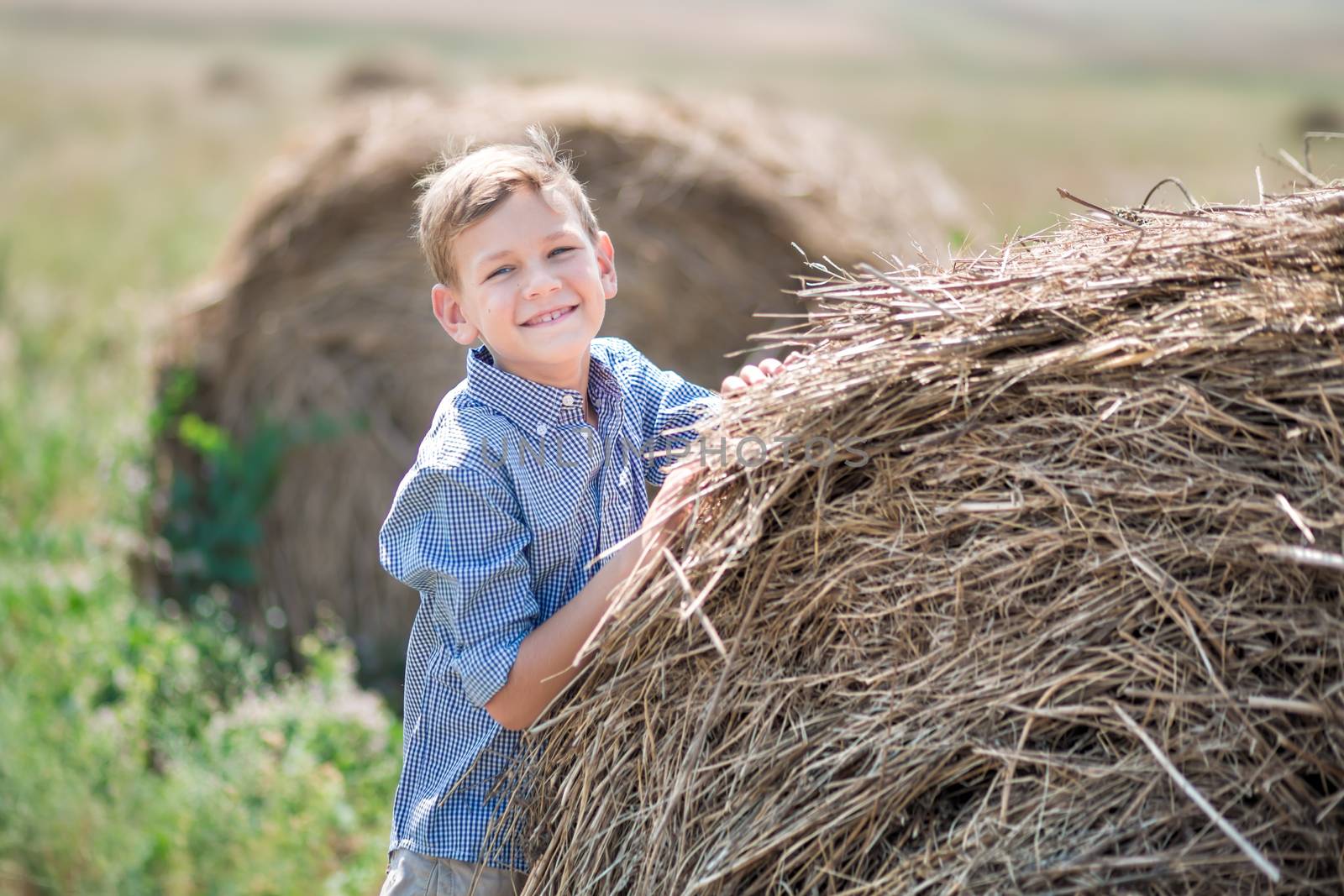 Attractive boy sitting on a haystack and smiling.