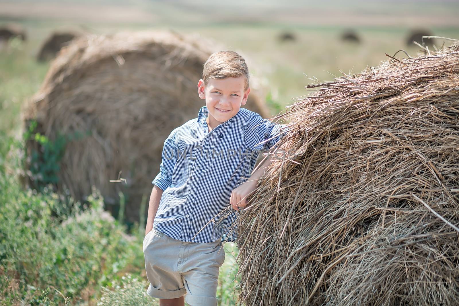 Attractive boy sitting on a haystack and smiling.