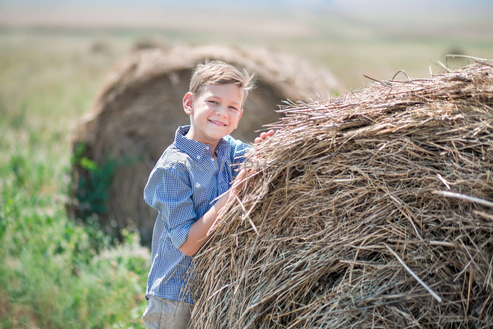 Attractive boy sitting on a haystack and smiling.