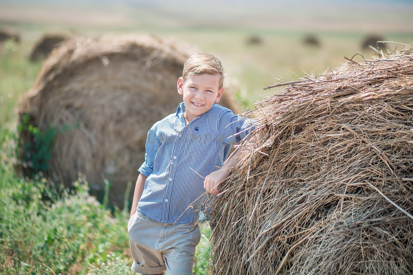 Attractive boy sitting on a haystack and smiling.