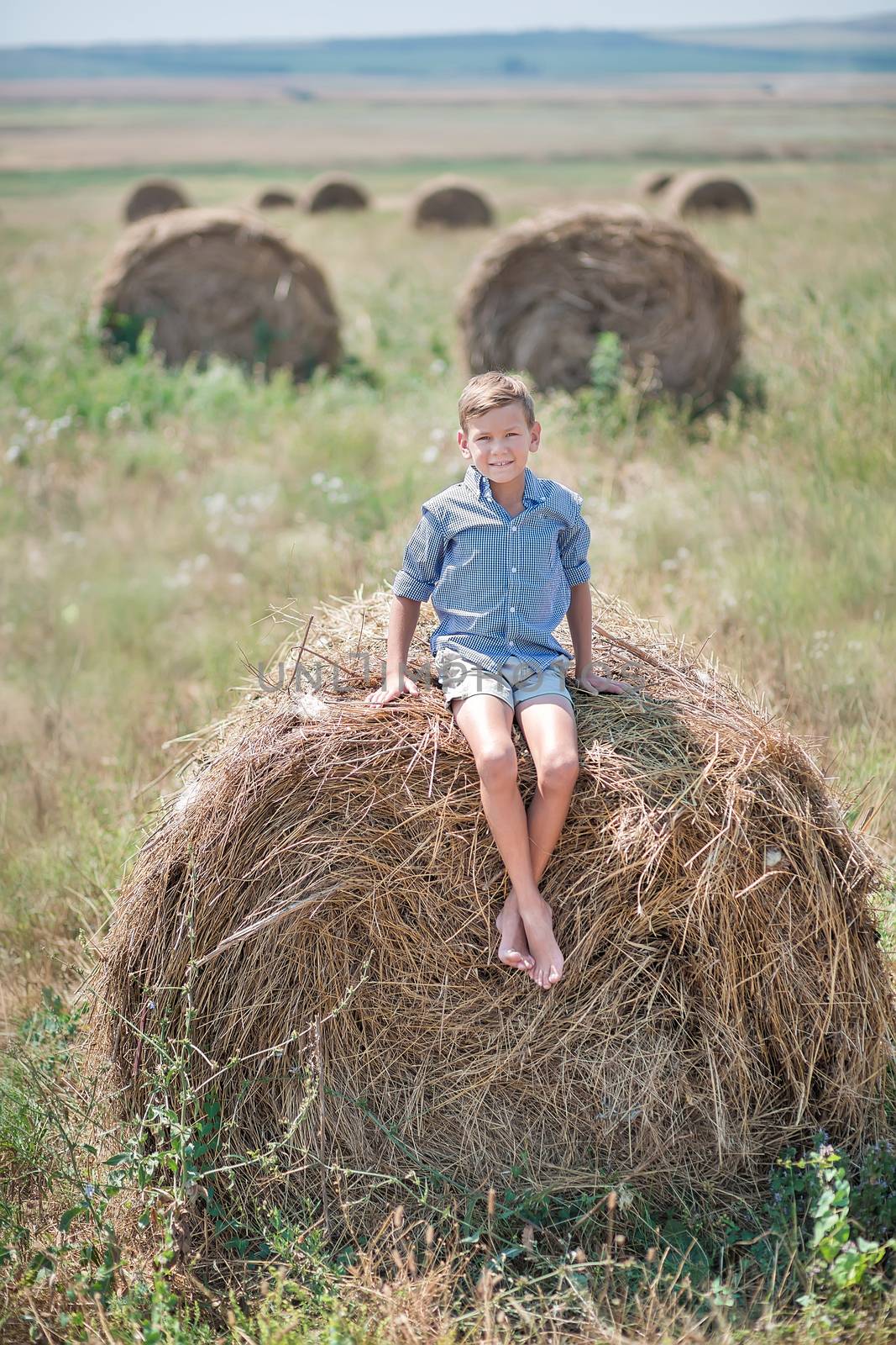 Attractive boy sitting on a haystack and smiling.