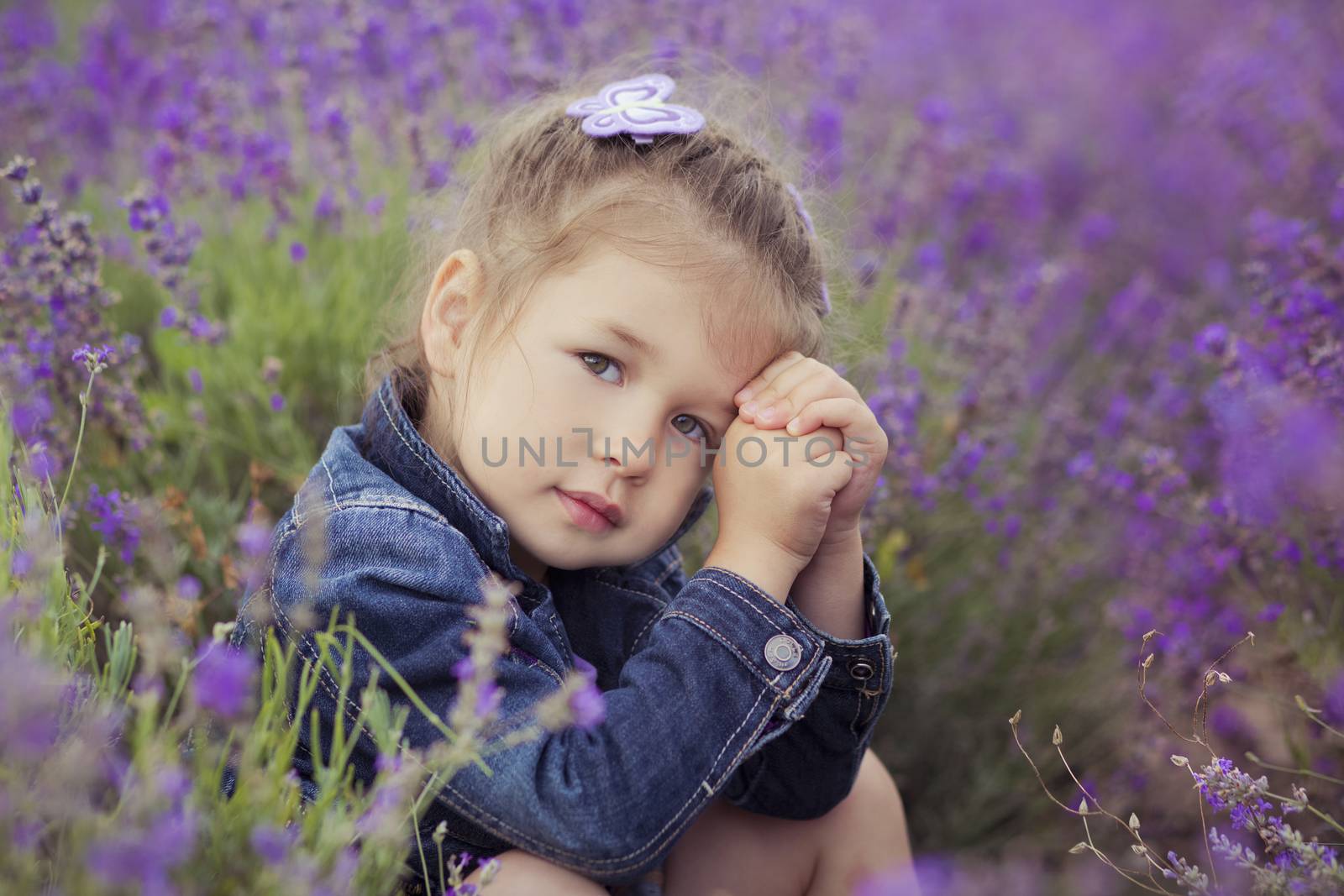 Pretty young girl sitting in lavender field in nice hat boater with purple flower on it