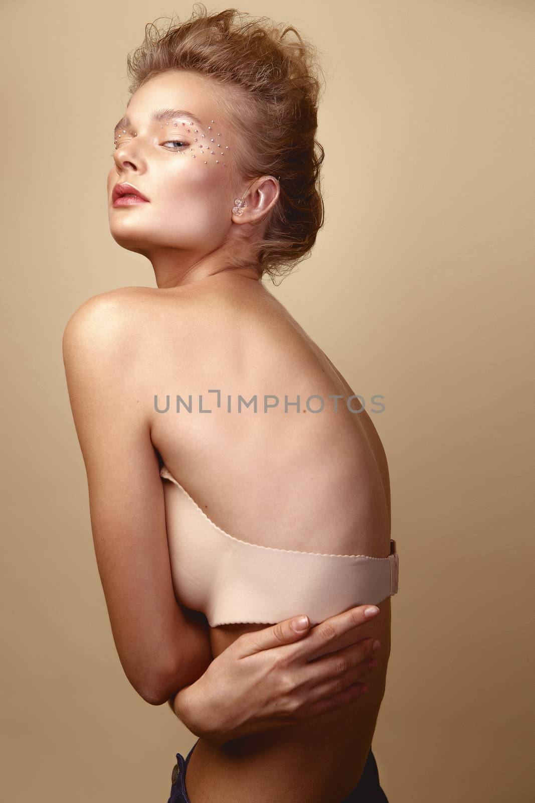 Studio Portrait of a young cute blonde model girl in art makeup with rhinestones