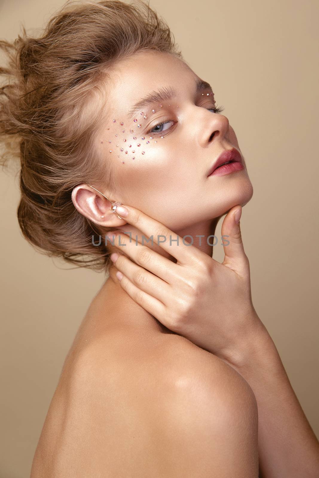 Studio Portrait of a young cute blonde model girl in art makeup with rhinestones