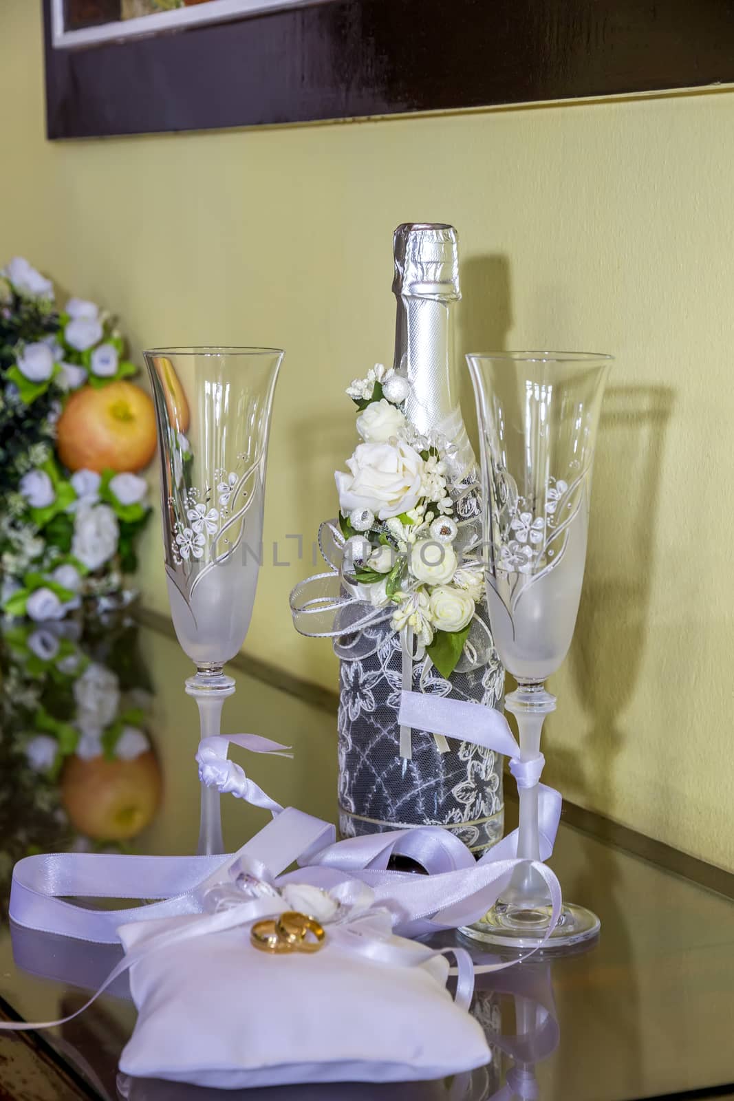 Wedding rings on beautiful pillows against the background of festive wine glasses and champagne. Wedding symbols, attributes.