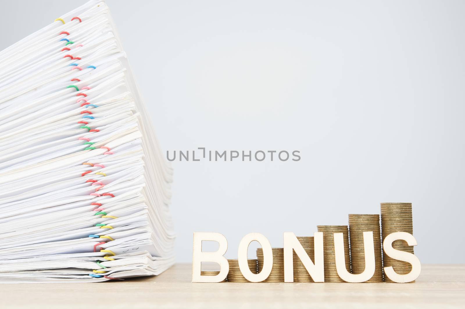 Bonus letters and step pile of gold coins with overload document report of sale and papercilp on wooden table with white background and copy space. Business and finance concept rich and successful.