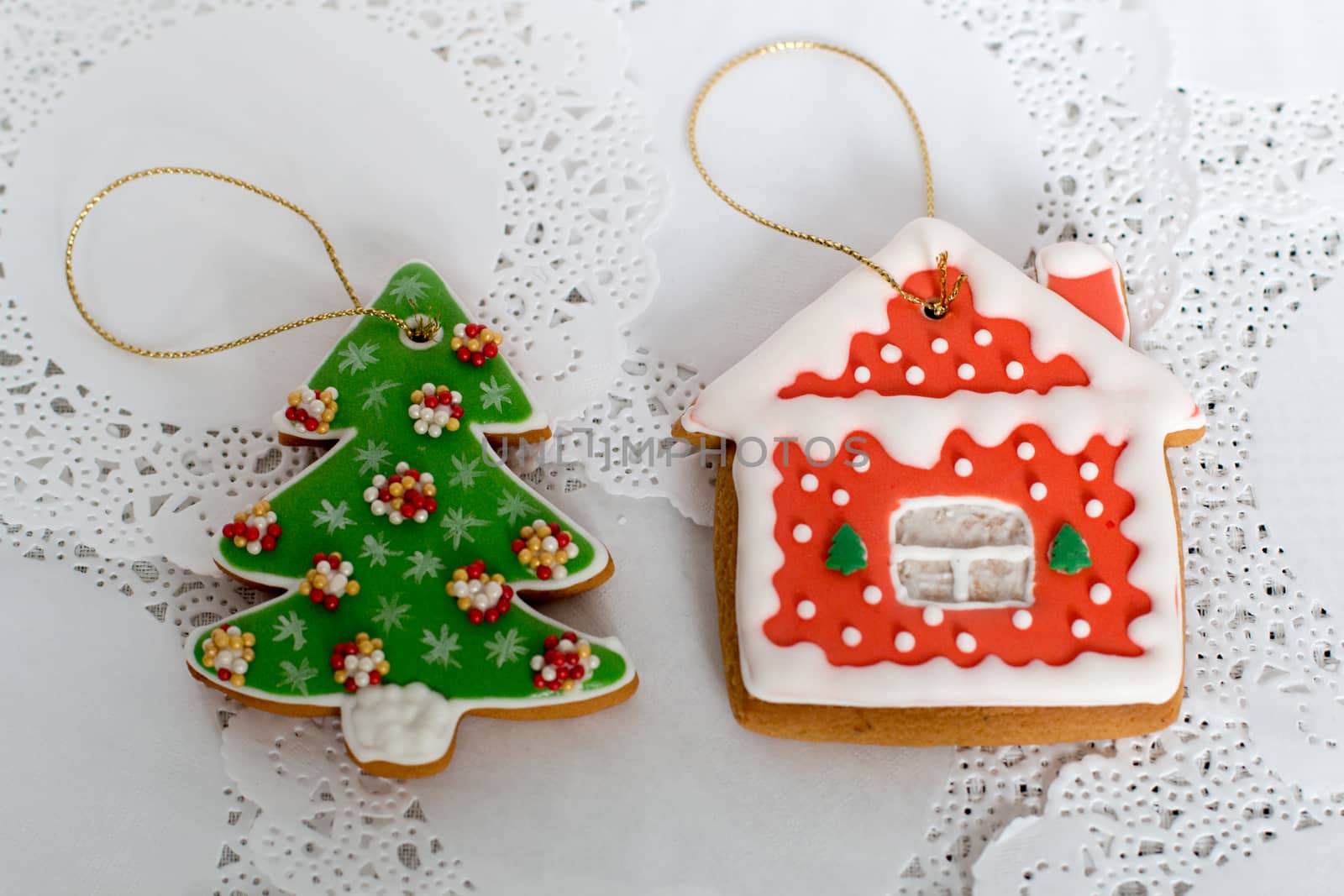 Two gingerbread cookies in the shape of the Christmas tree and small house on a white napkin background. Top view, flat lay, copy space