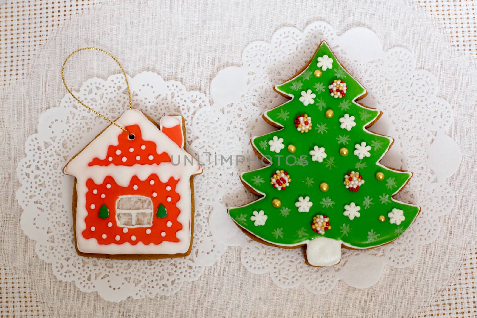 Two gingerbread cookies in the shape of the Christmas tree and small house on a white napkin background. Top view, flat lay, copy space