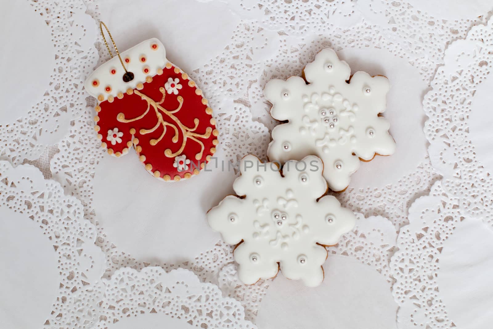 Three gingerbread cookies in the shape of red mitten and two snowflakes on a white napkin background. Top view, flat lay, copy space. Curly Christmas gingerbread home cooking