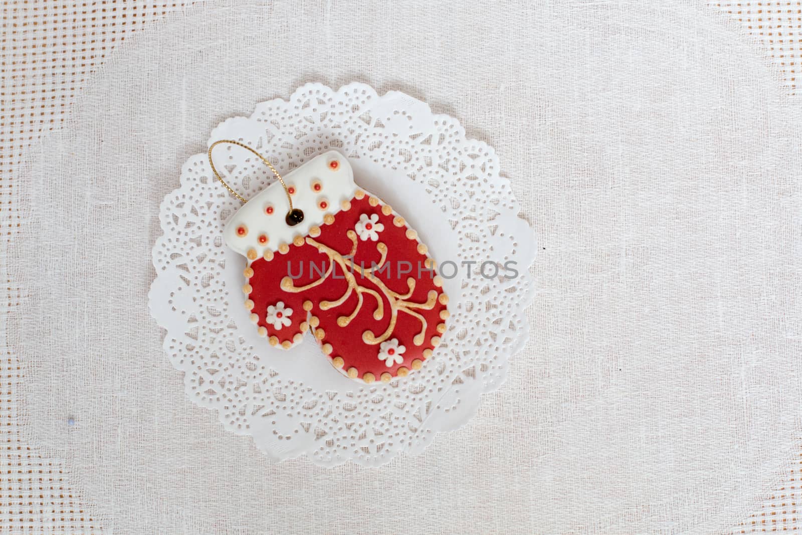 Gingerbread cookie in the shape of red mitten on a white napkin background. Top view, flat lay, copy space. Curly Christmas gingerbread home cooking. Christmas toy