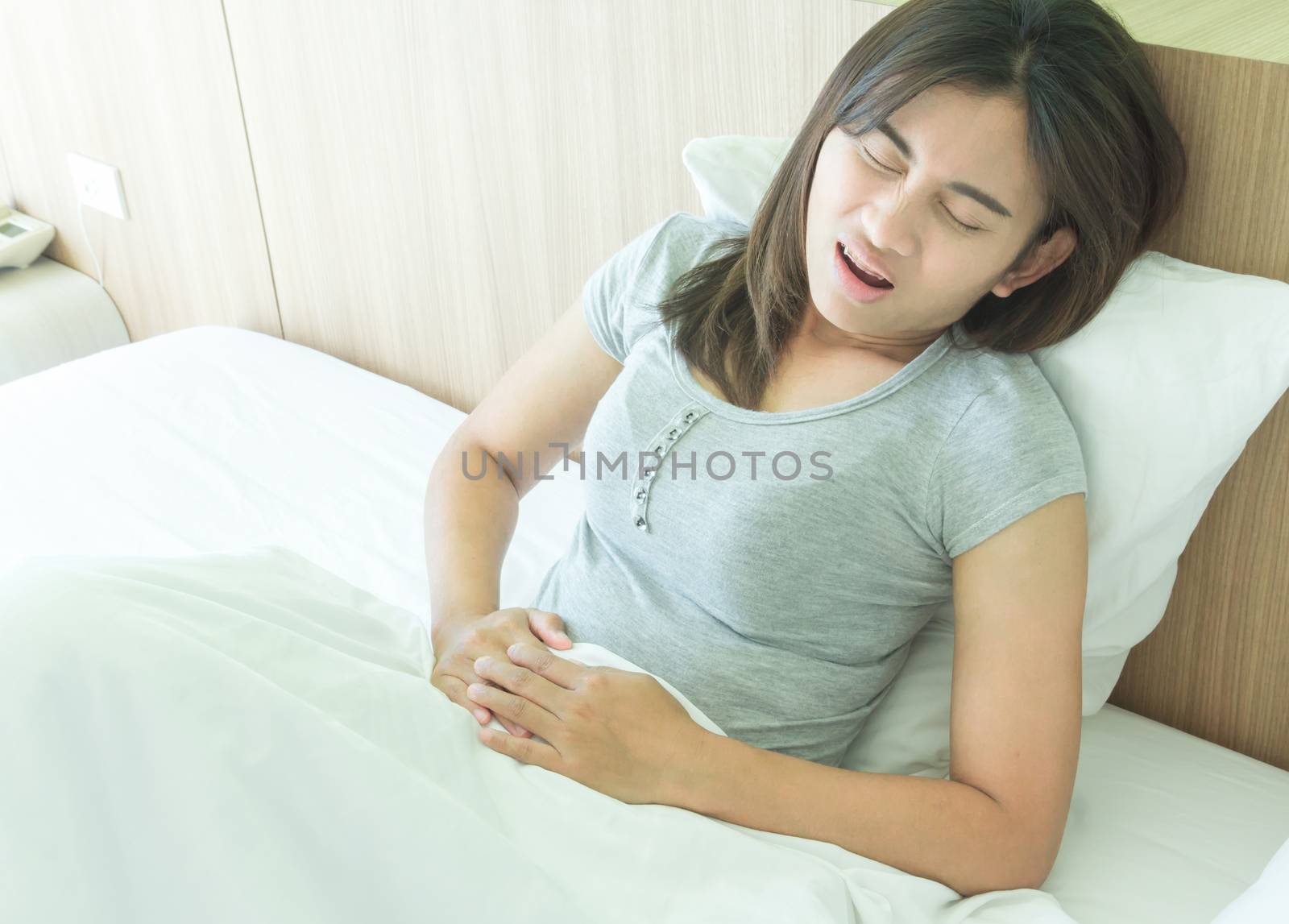 Closeup woman hand holding abdominal with stomach ache lying on bed, health care and medical concept