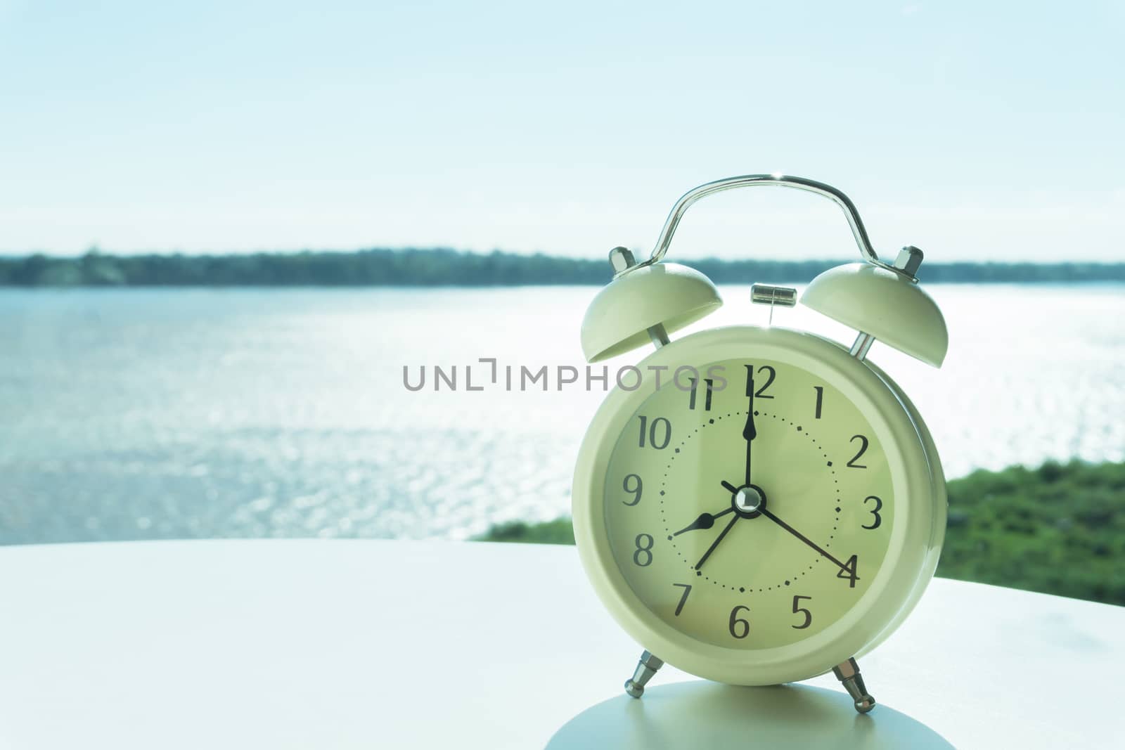 Alarm clock on white table with river and nature background, morning relax time concept