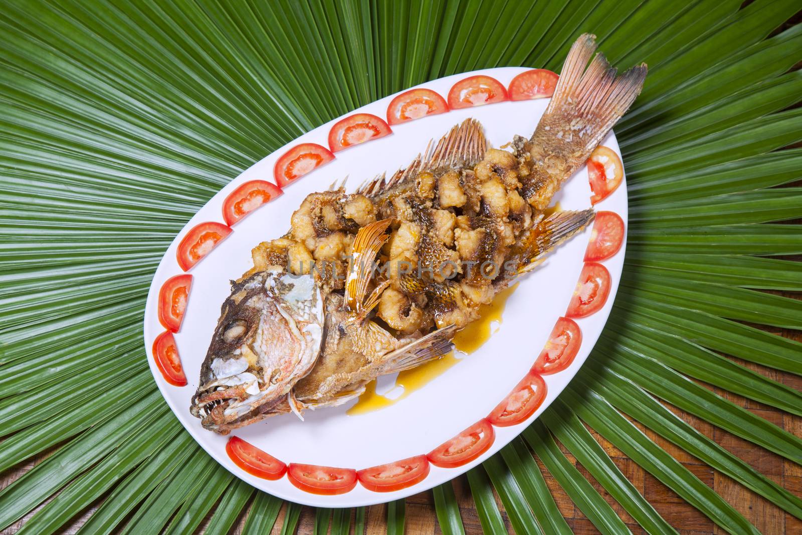 Fried snapper topped with sweet fish sauce with herbs,Plate with tomato.