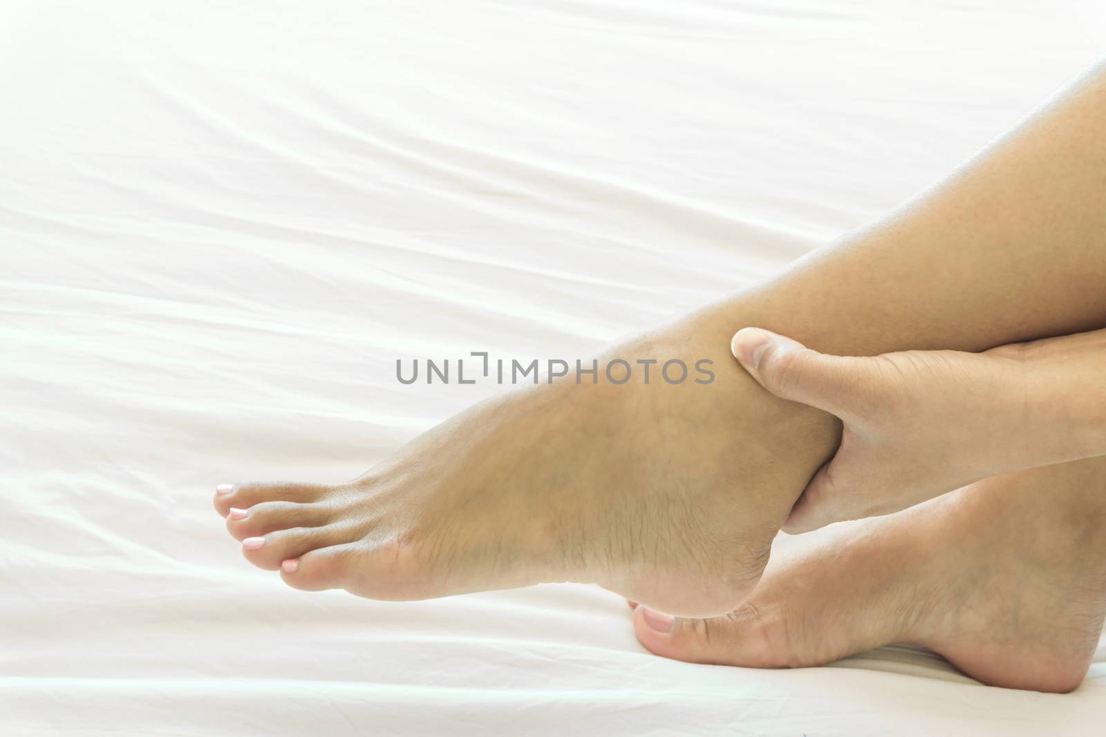 Woman hand holding ankle with pain on white bed, health care and by pt.pongsak@gmail.com