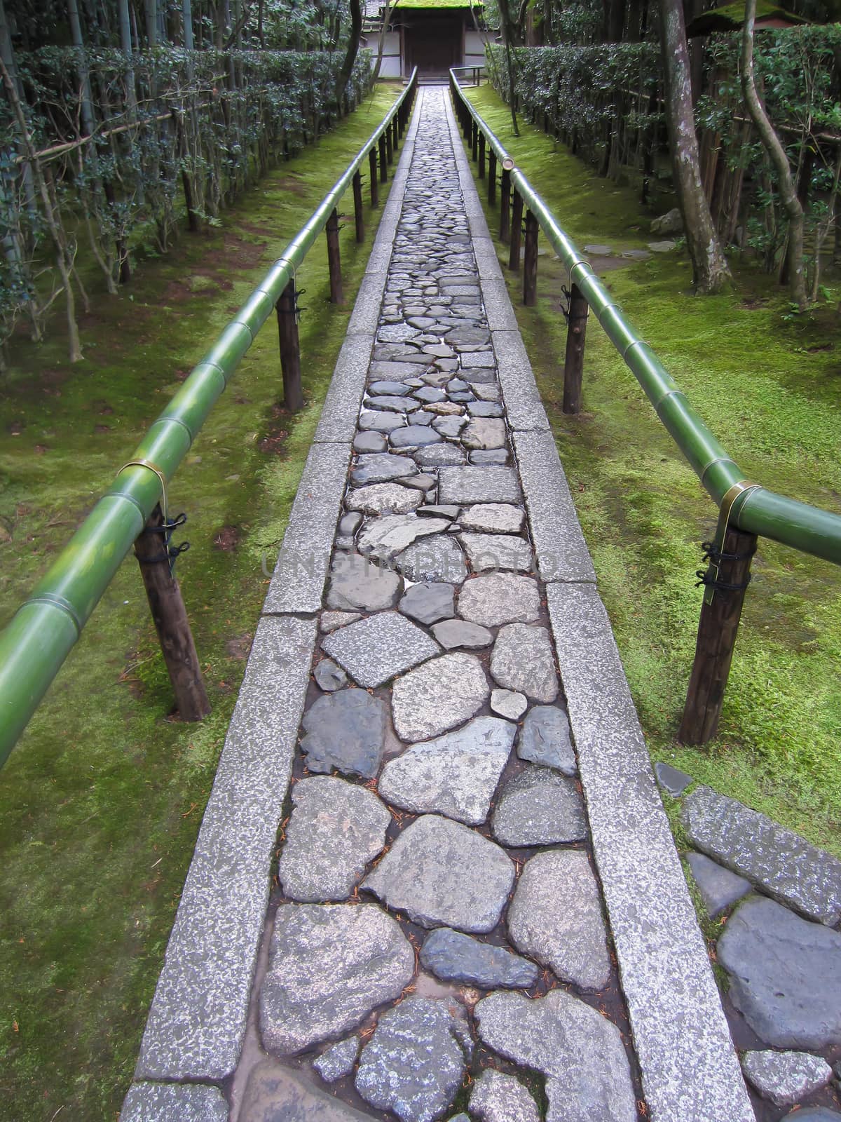 Long pathway made of stone leads through a green Japanese garden towards a temple entrance on a bright day in Kyoto.