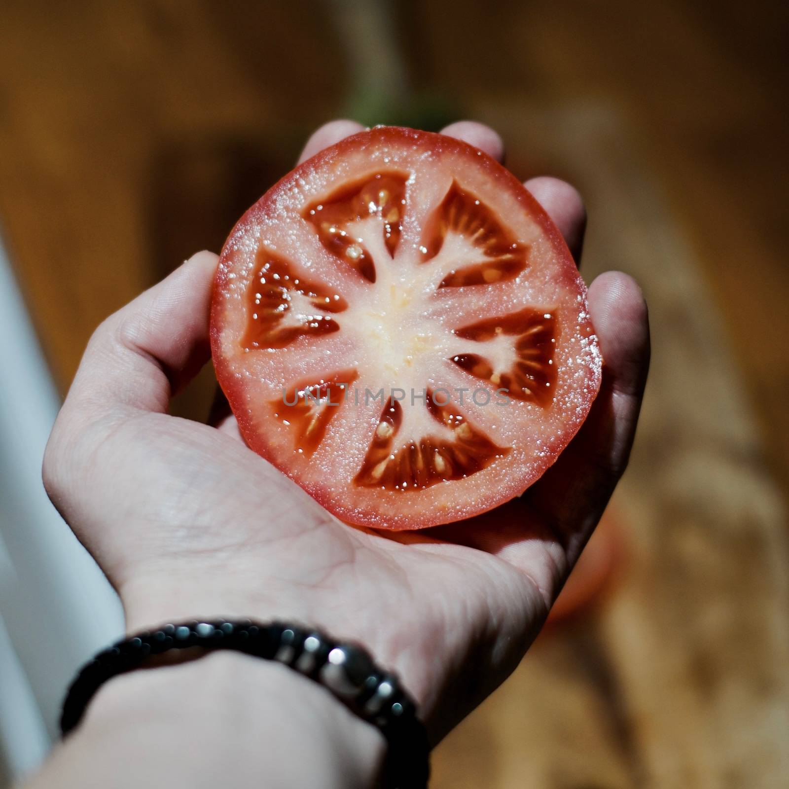 Red delicious fresh tomato in man hand with black bracelet. Kitchen concept.