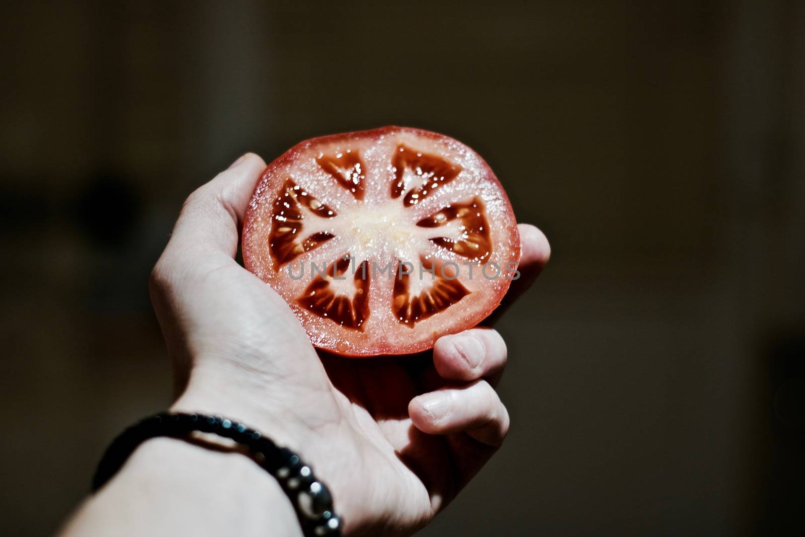 Red delicious fresh tomato in man hand with black bracelet. Kitchen concept.
