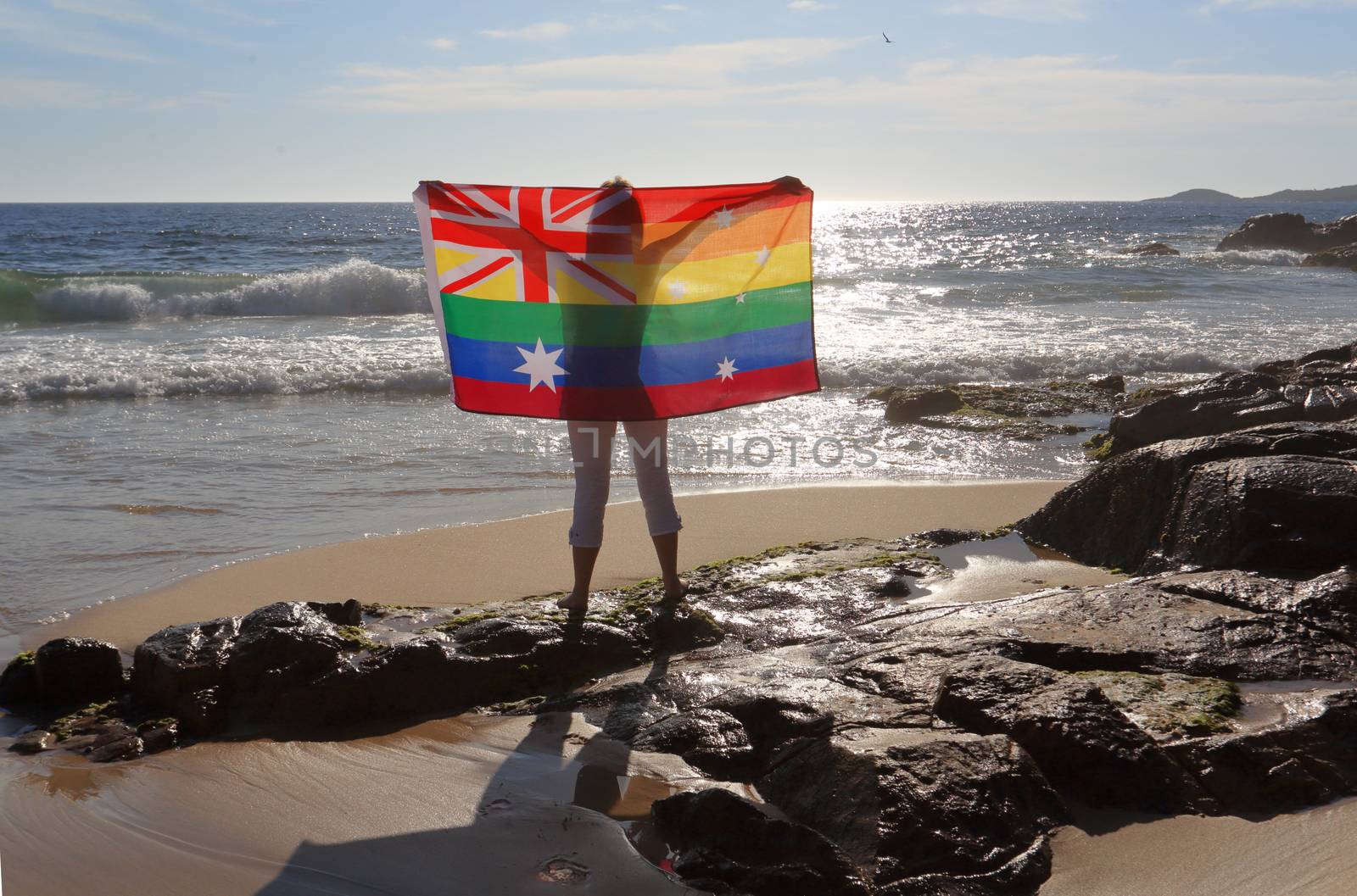 On November 15 Australia voted yes to Marriage Equality.  A woman holding an Australian flag in rainbow colours by the ocean