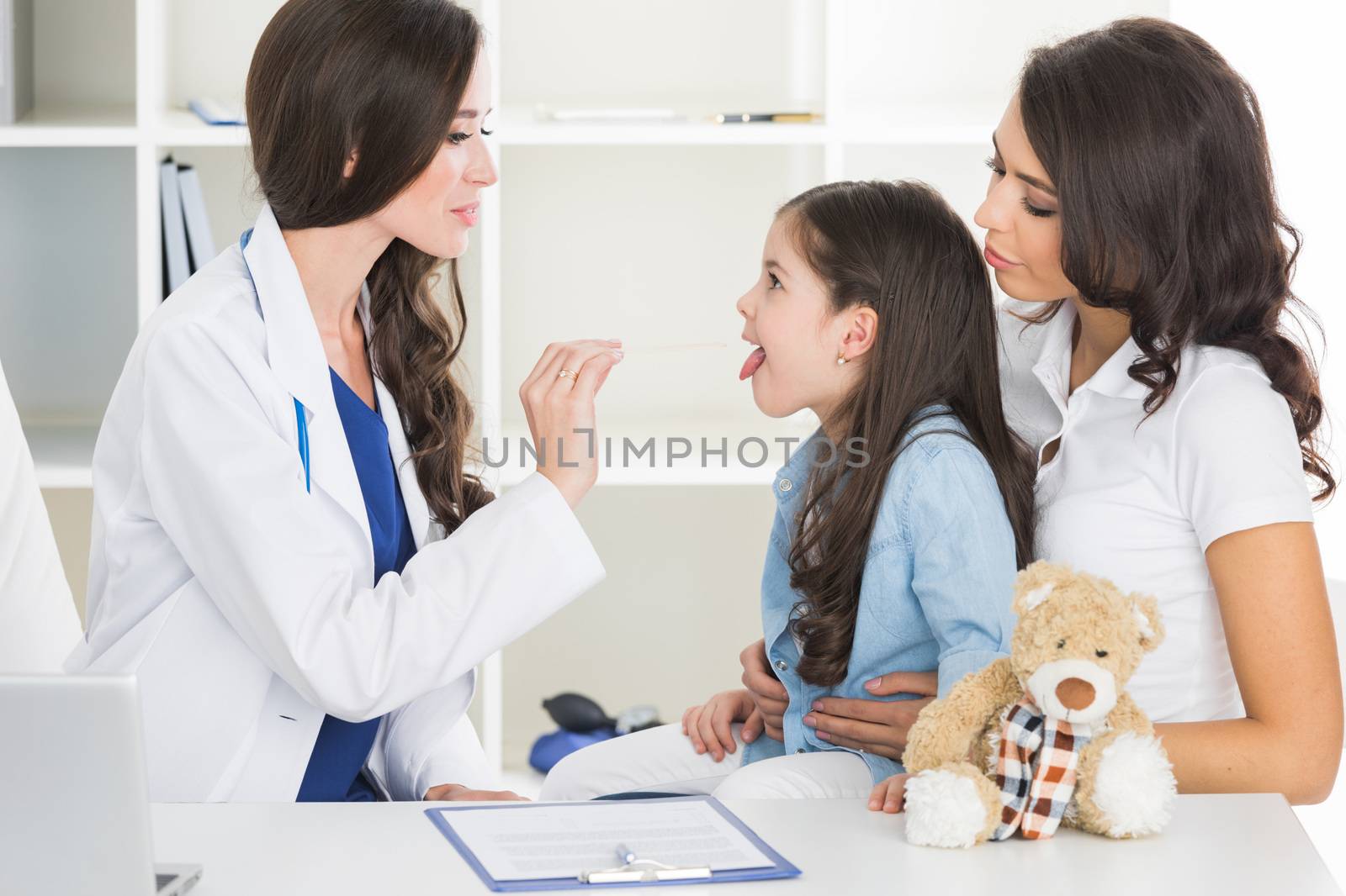 Little girl and her mother at pediatrician office. Doctor examine child's throat