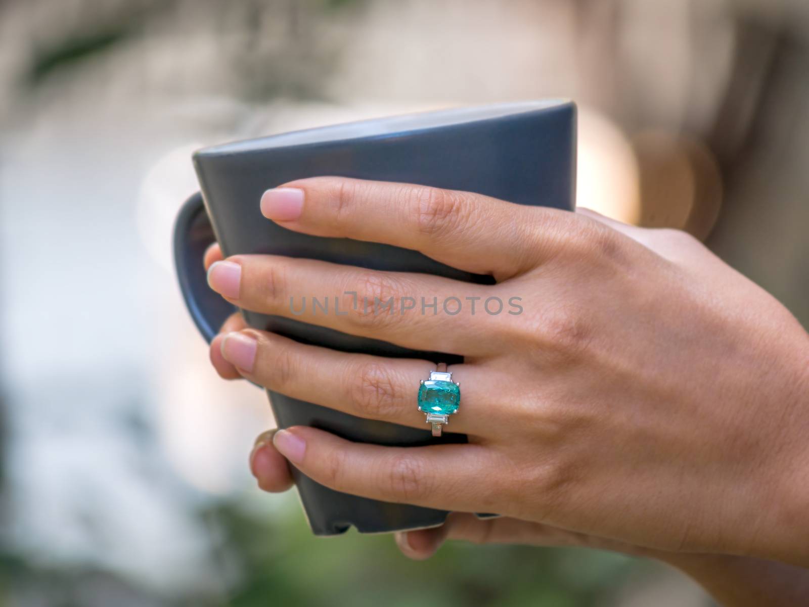 Closup female hand holding coffee cup and wearing green gem ring with white diamond on finger