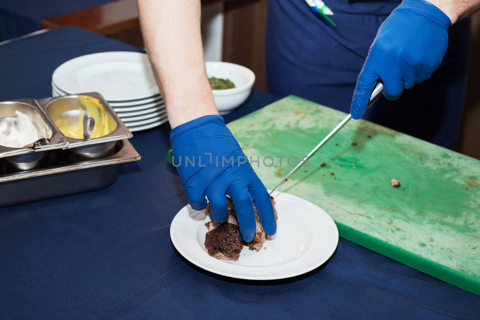 Young white chef in kitchen interior. Man marinating beef steak on a tray. Meat ready for the grill and serve. Only hands by 3KStudio