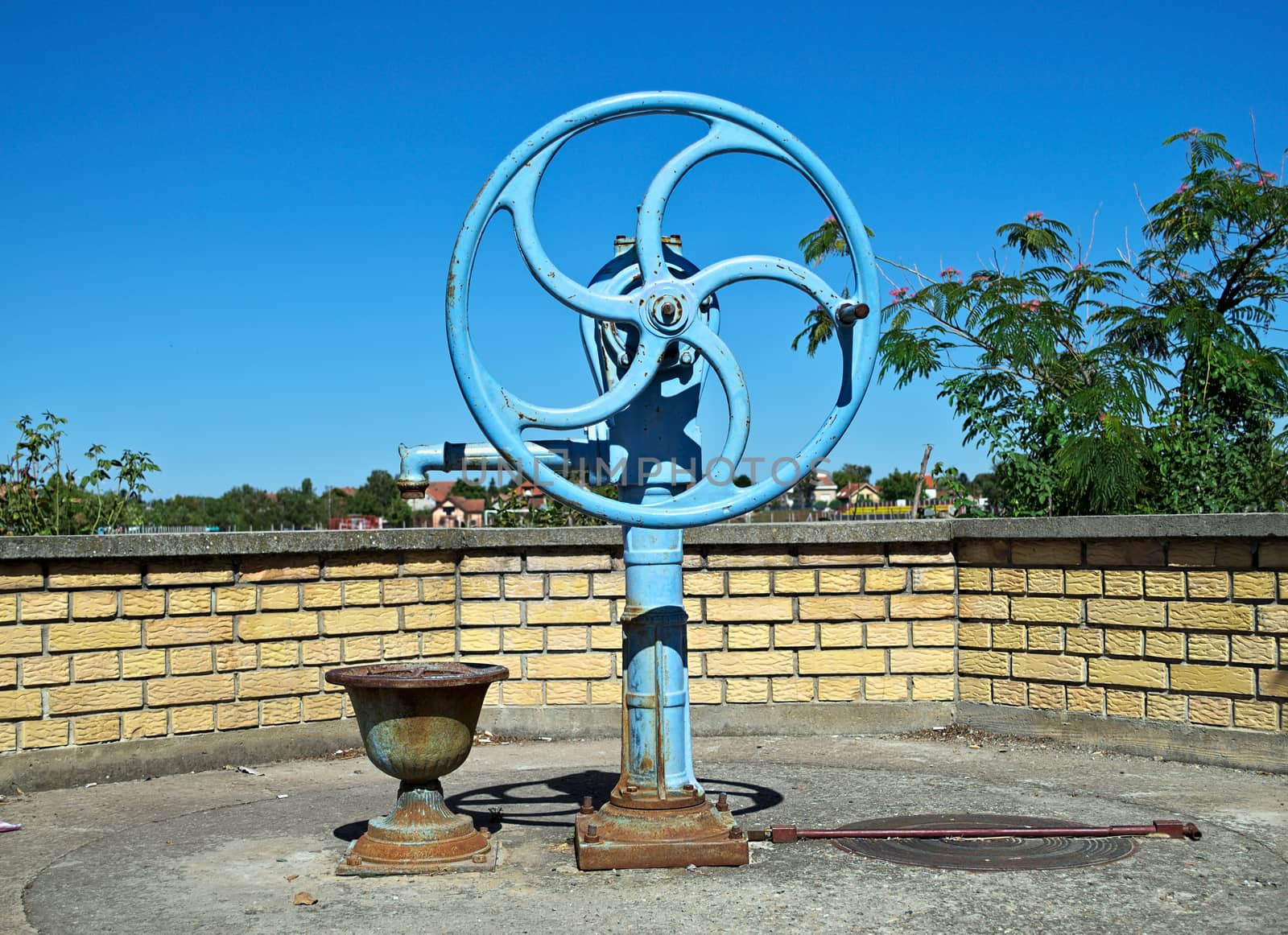 Blue water well pump, with wheel, on summer sun