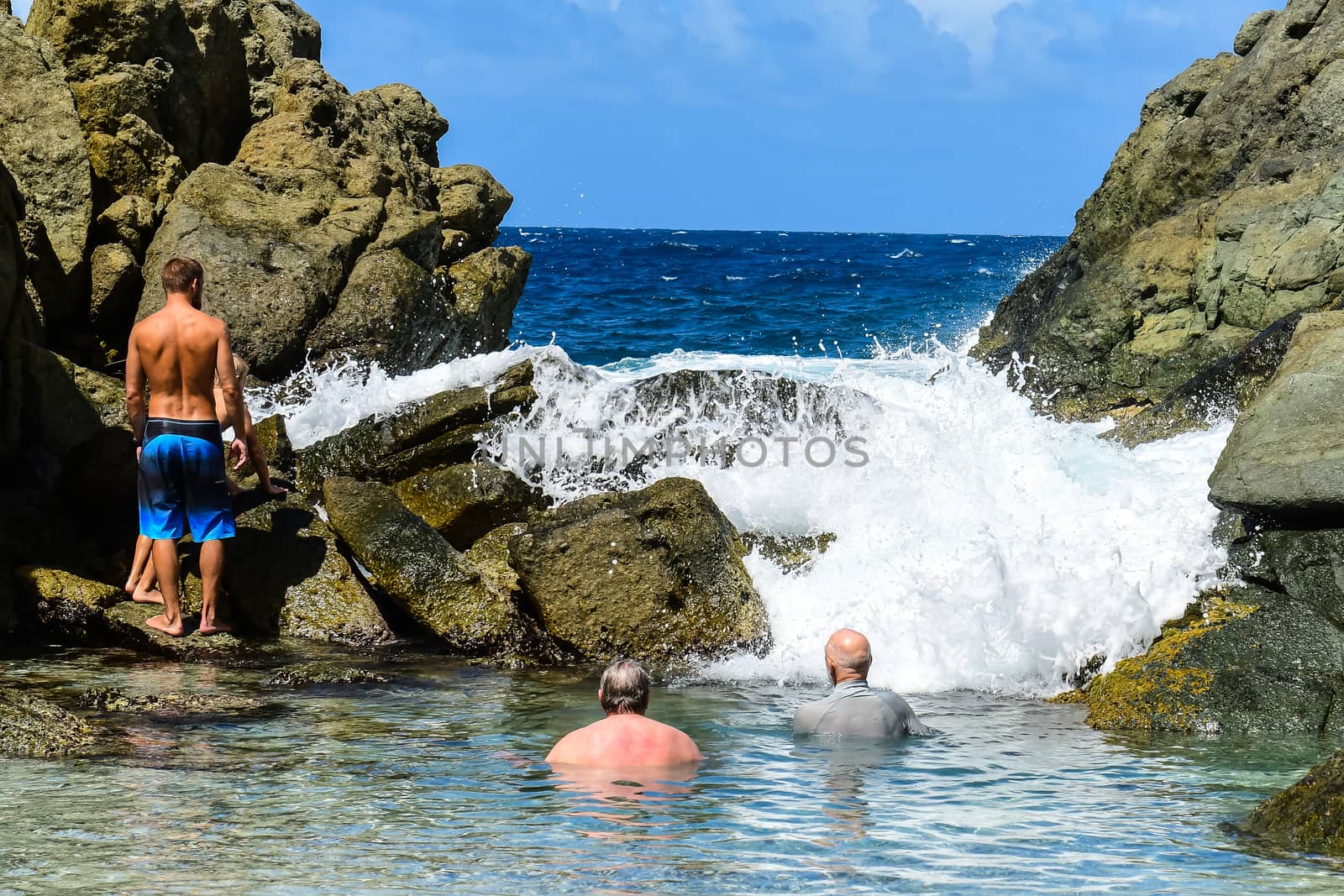 Bathers enjoying the surf rolling over the rocks in the Bubble Pool on Jost Van Dyke in the British Virgin Islands.