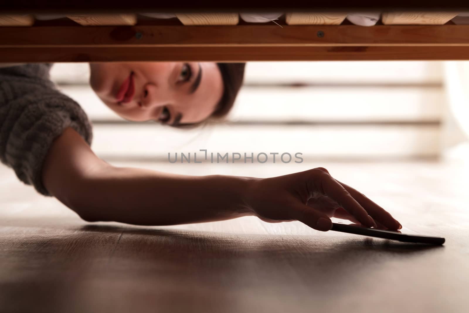Closeup shot of girl who takes a smarthone from under the bed
