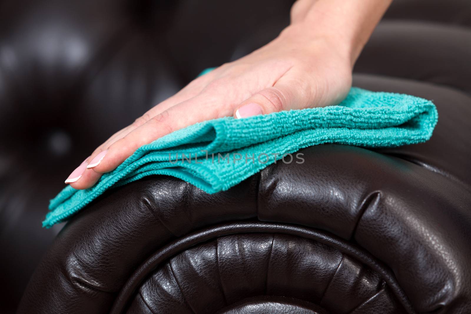 Closeup shot of female hand wiping brown leather couch of sofa