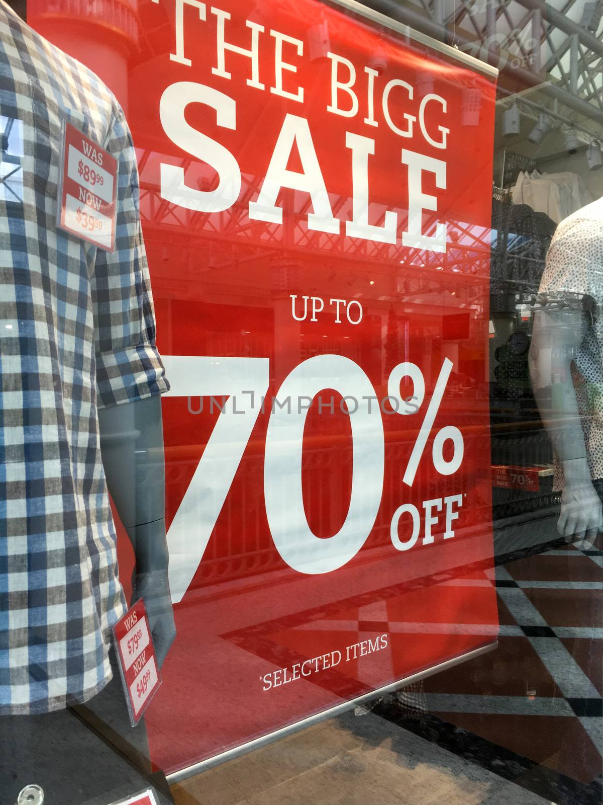 Mens fashion boutique Sale Sign showing markdowns up to 70% in shop front window with mannequins