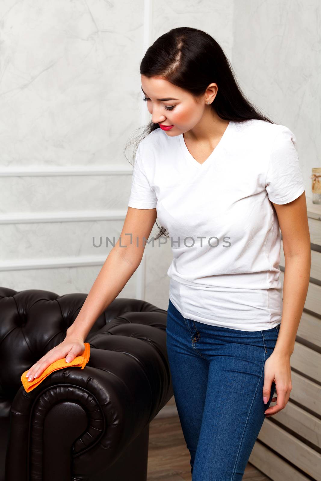 Young brunette woman cleaning dark brown chester leather sofa wi by Nobilior