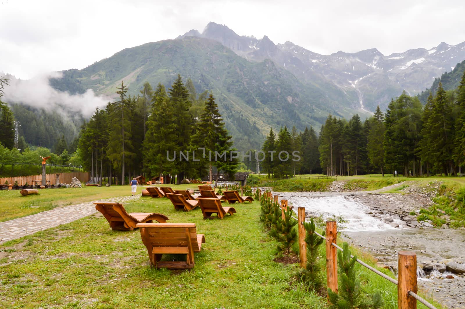 Deck chairs lined up facing the mountain and a torrent in a park in the dolomites in Italy