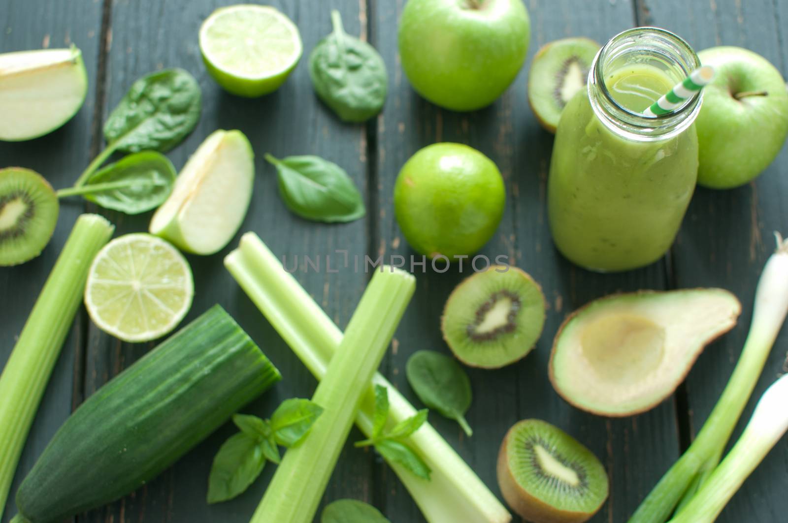 Fresh ingredients around a green smoothie bottle with straw