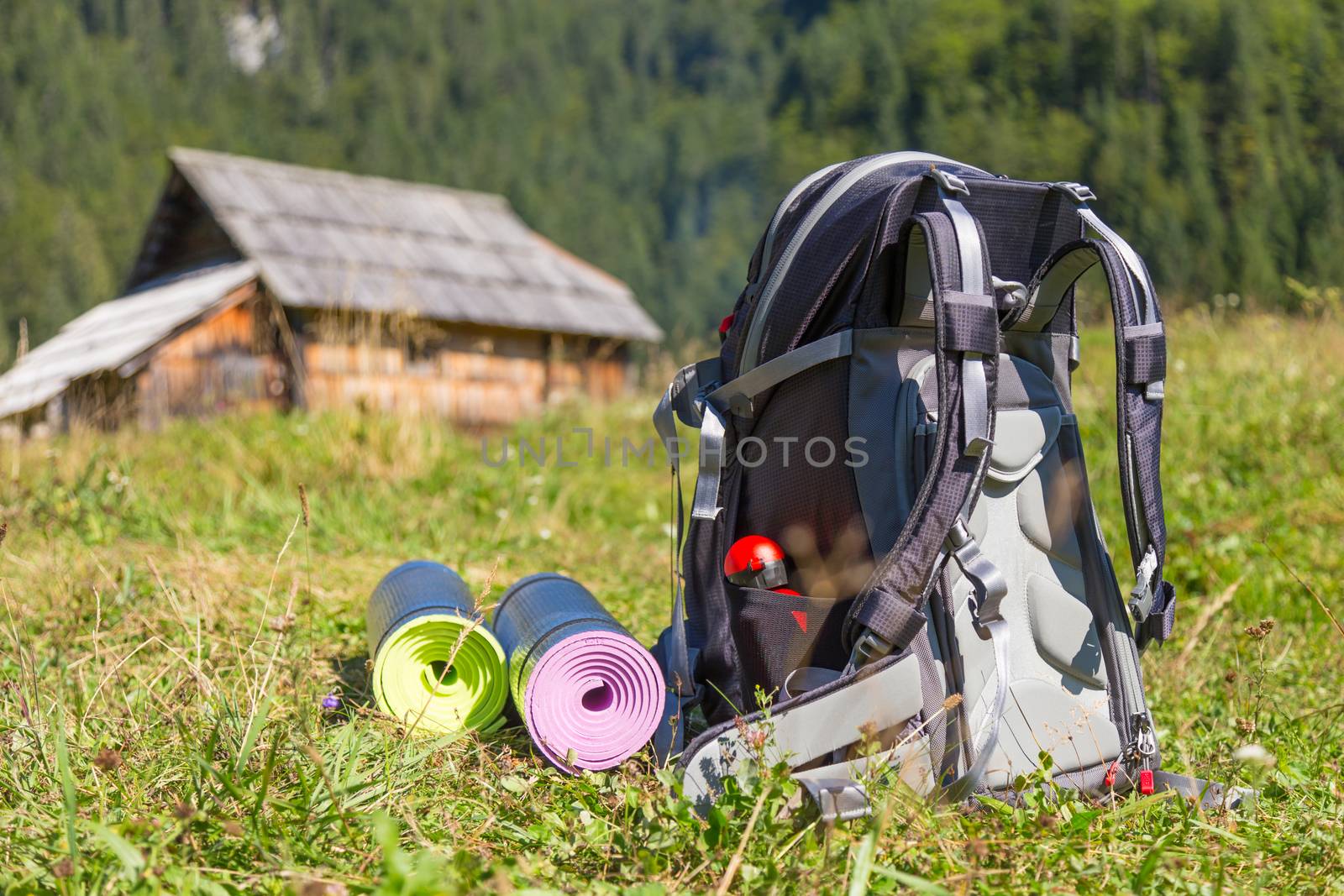 Backpack and yoga mats on mountain meadow with traditional wooden shepherd's huts, Alps, Slovenia.