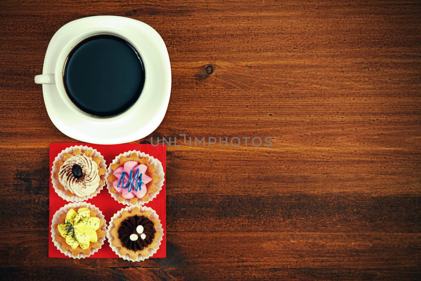Cup of tea or coffee and four cupcakes on brown table. Top veiw by Nobilior