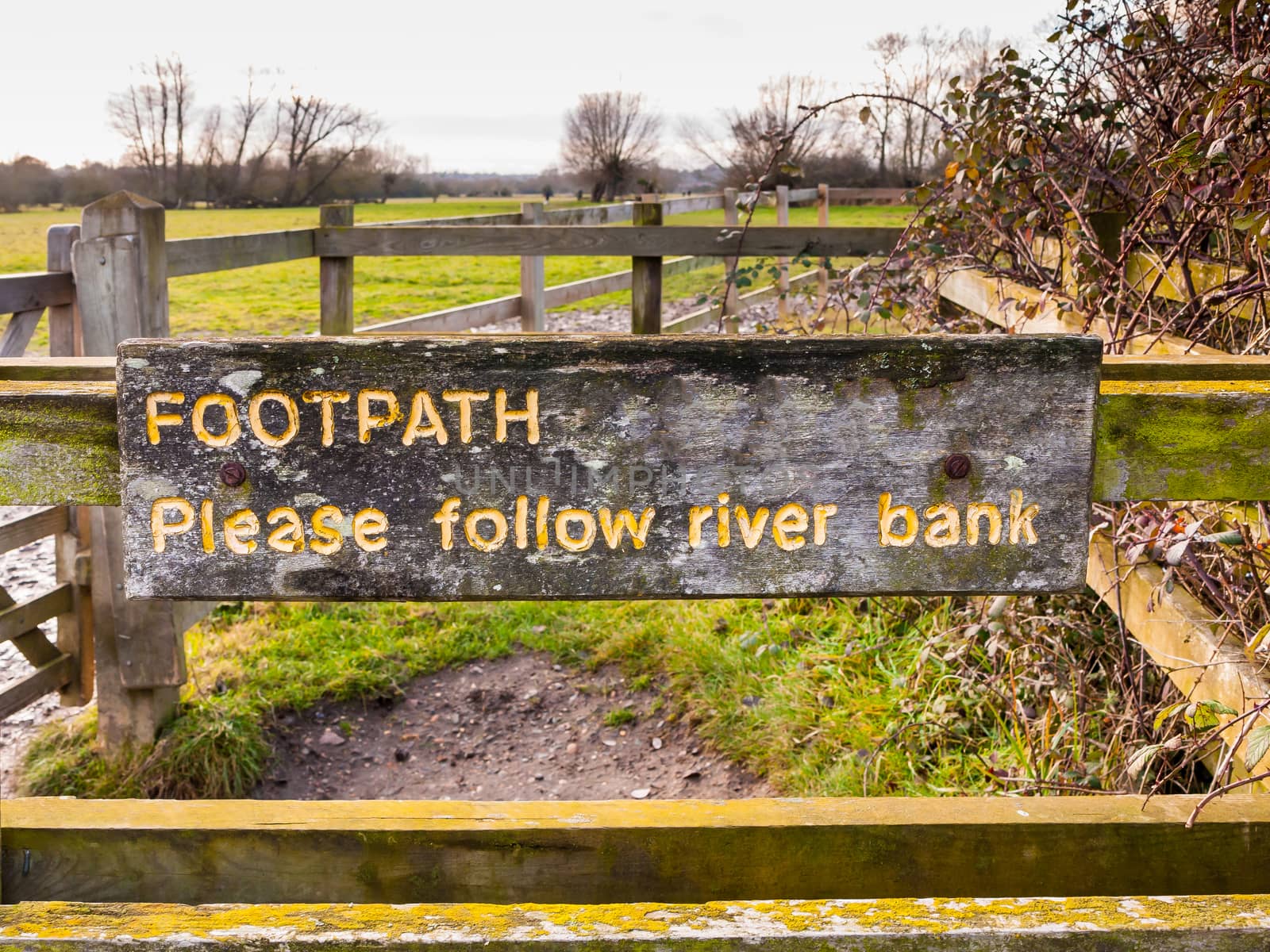 footpath please follow river bank yellow painted engraved wooden fence sign close up; essex; england; uk