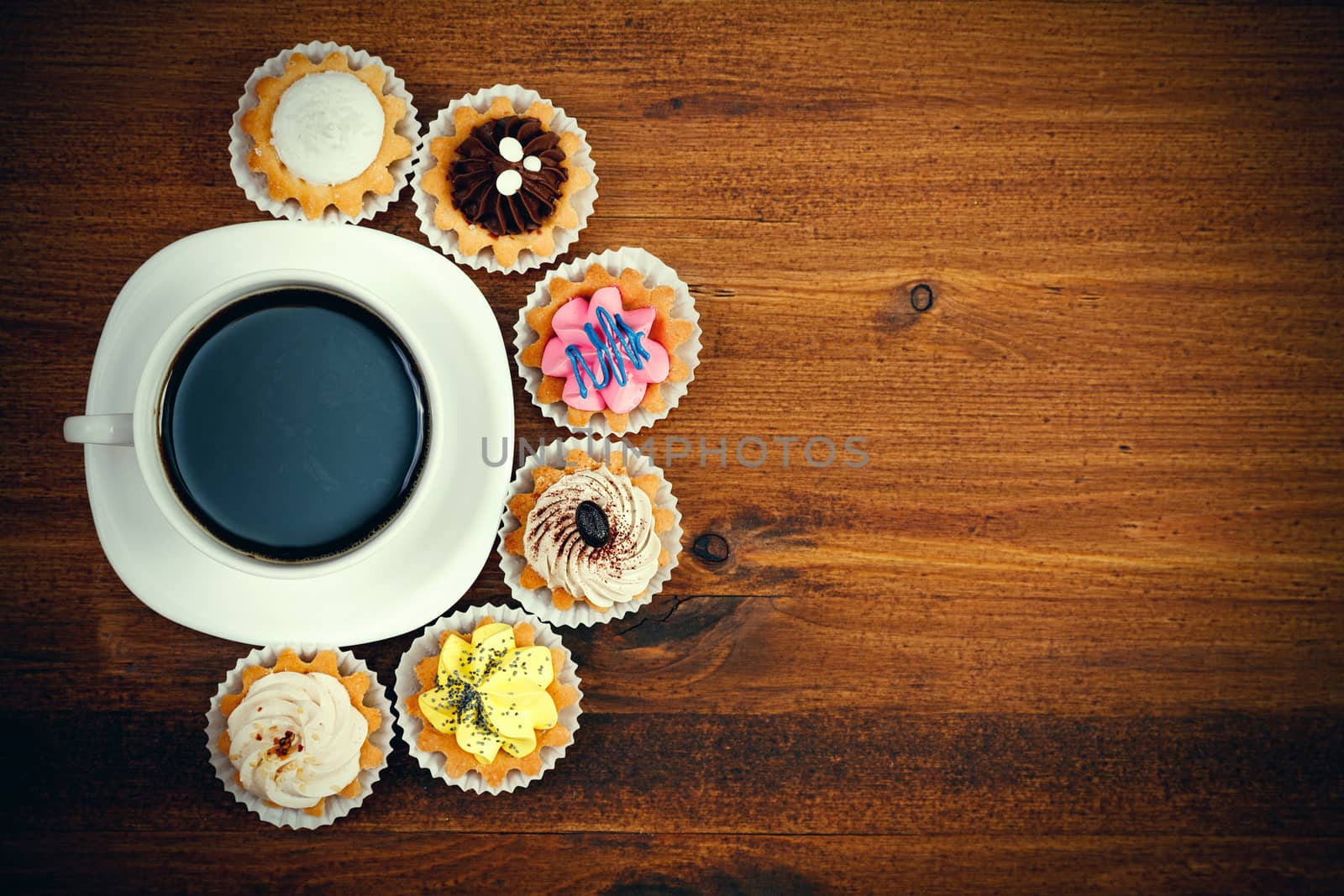 Closeup shot of small cup of coffee with colorful cupcakes. Flat lay style