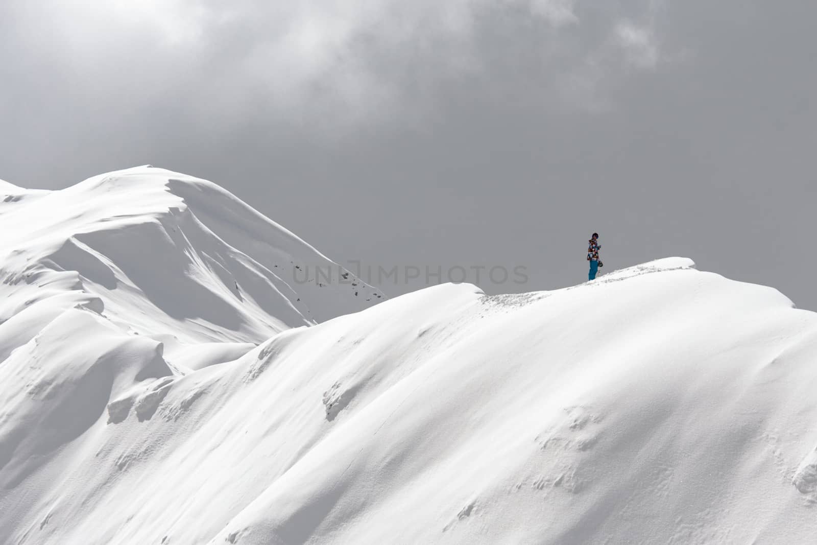 A stranded man on the snowy ridge of a mountain holding a cell phone trying to call