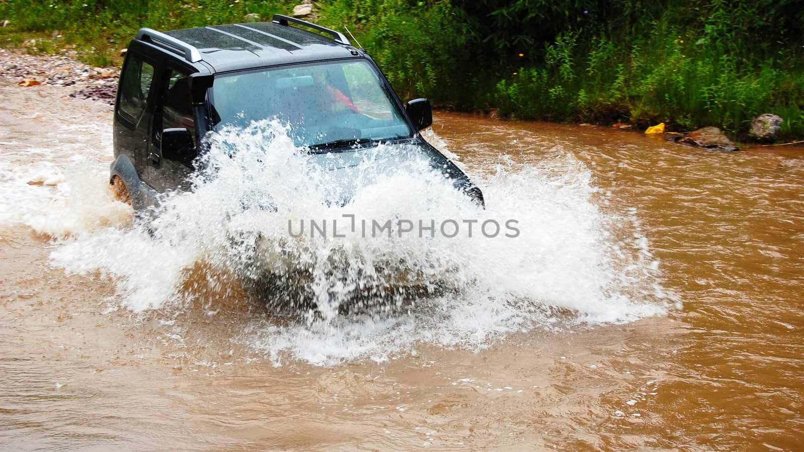 Off road vehicle crossing a deep stream of muddy water with big splash on the hood