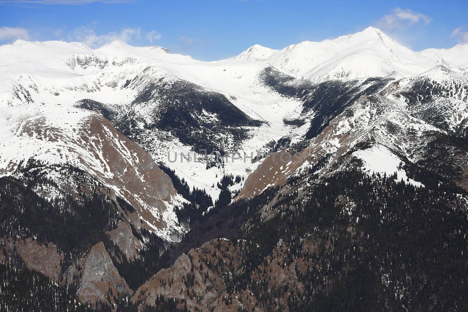 A beautiful view of high altitude peaks covered in snow and a nice valley in the middle starting between two rocky ridges with no snow left and continuing to the top of the mountains