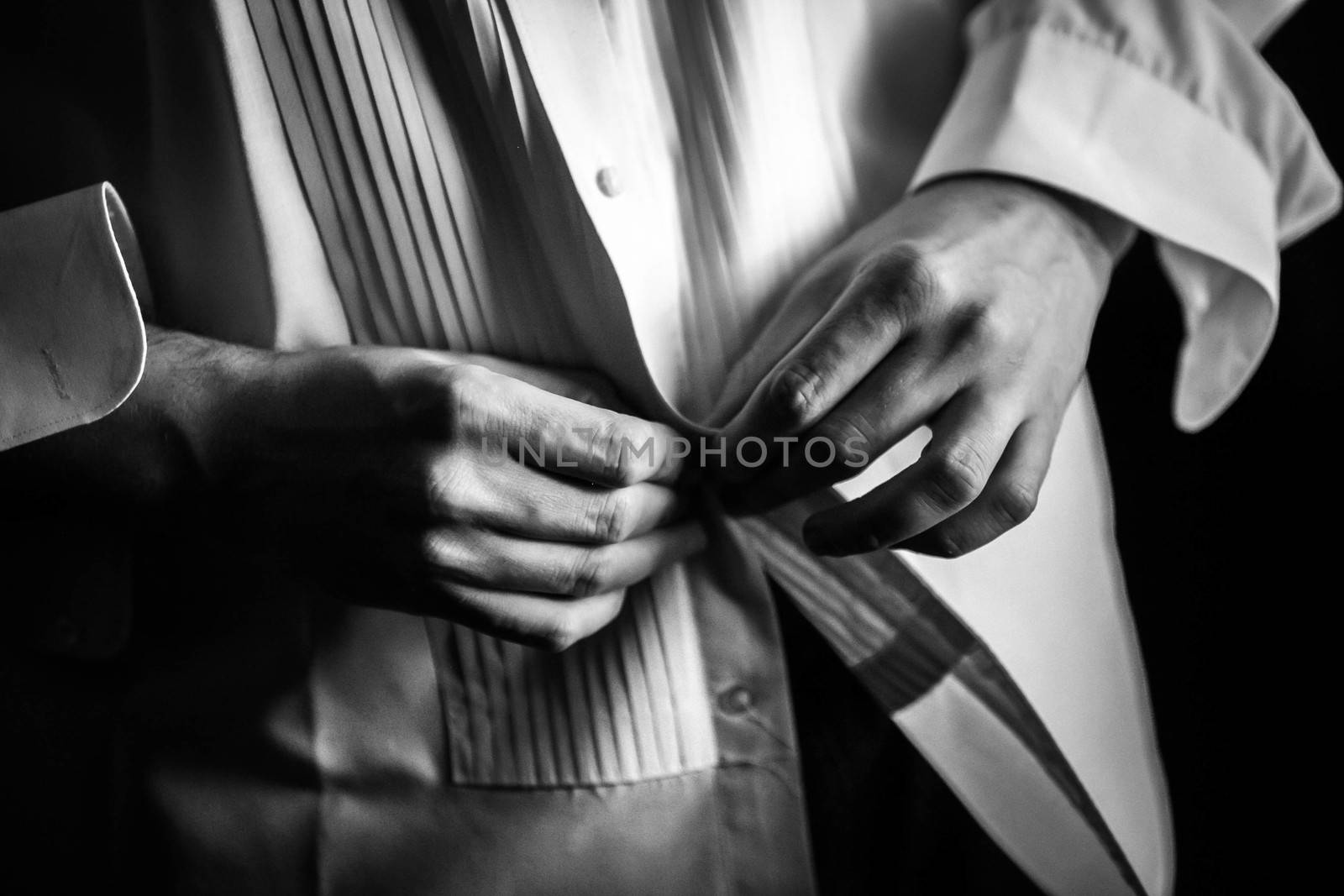 Black and white photo of a man buttoning his dress shirt.
