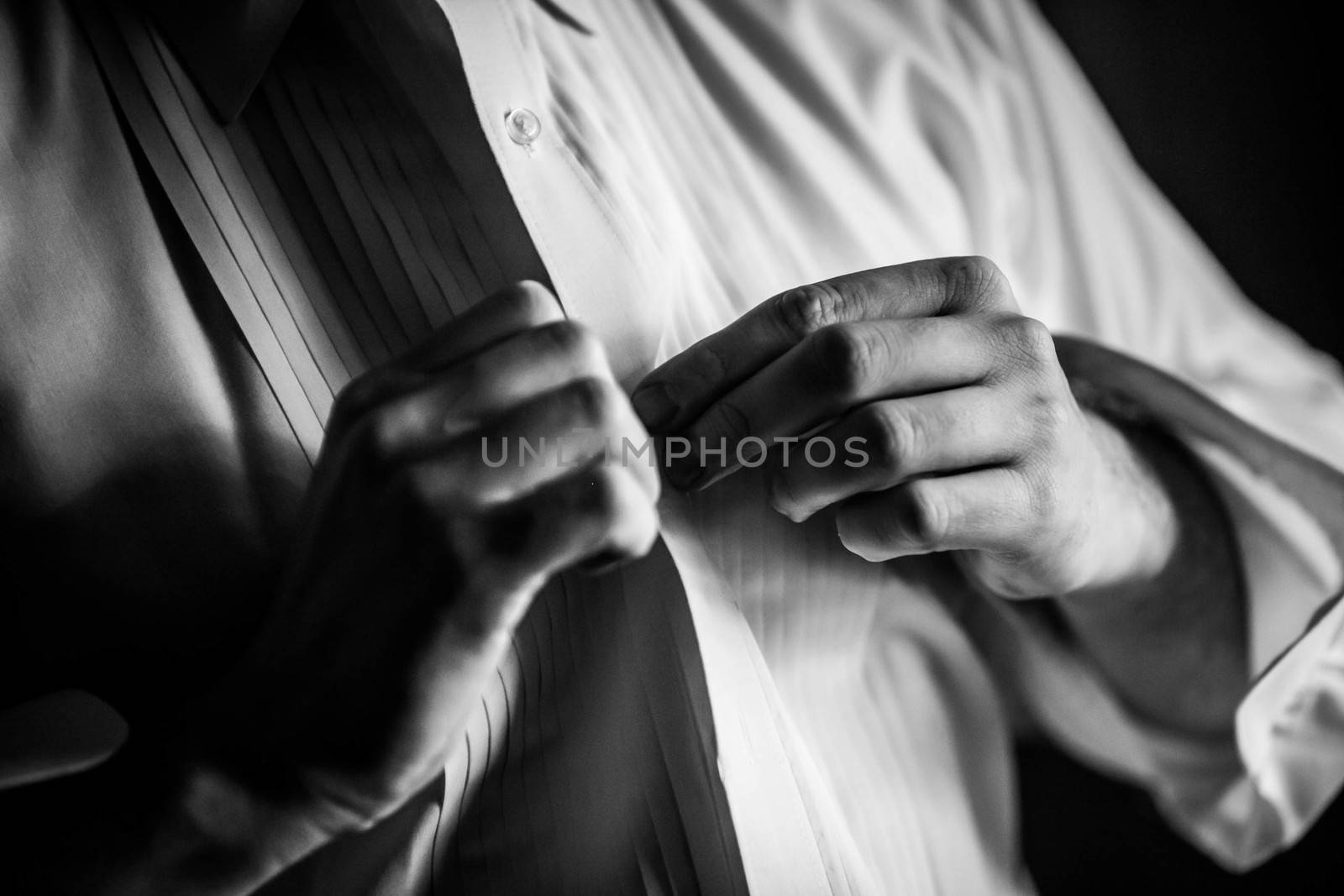 Black and white photo of a man buttoning his dress shirt.