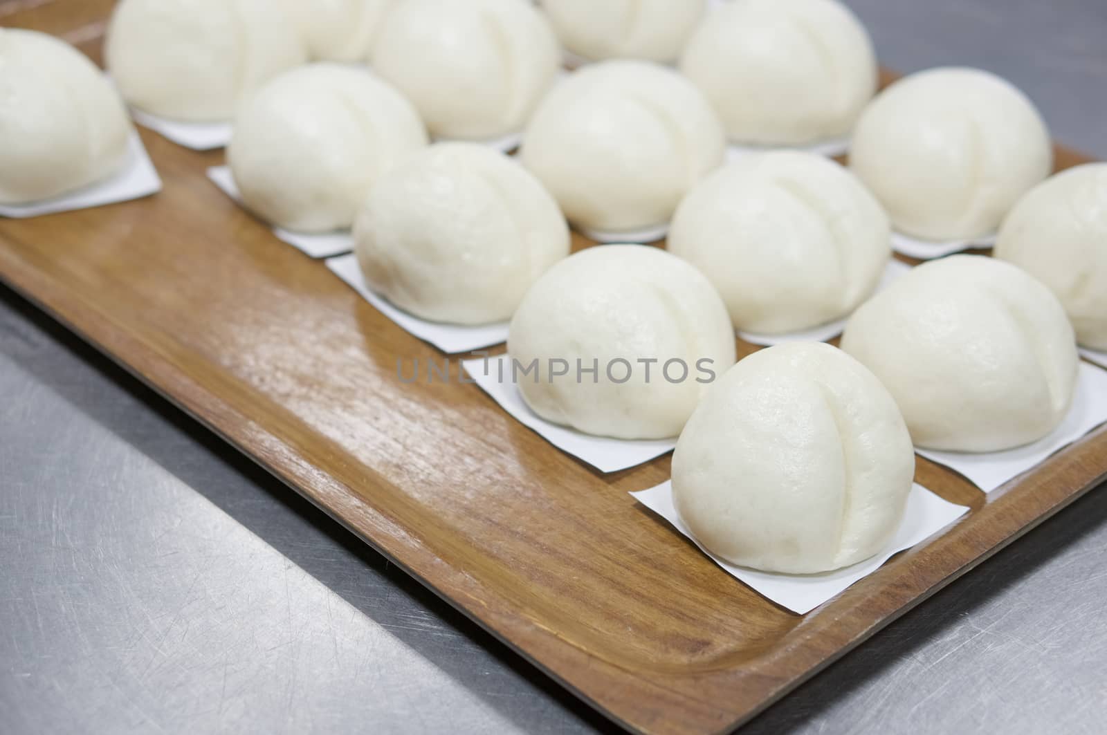 Close up steamed bun or dim sum on white paper in brown wooden tray have aluminium table as background at restaurant kitchen with copy space. Food and healthy concept photography.