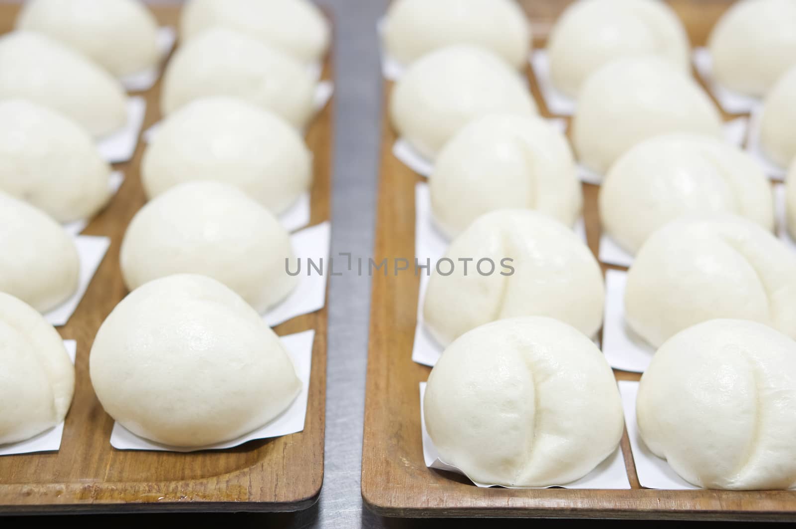 Close up steamed bun or dim sum on white paper put in a row in brown wooden tray have aluminium table as background at restaurant kitchen. Food and healthy concept photography.