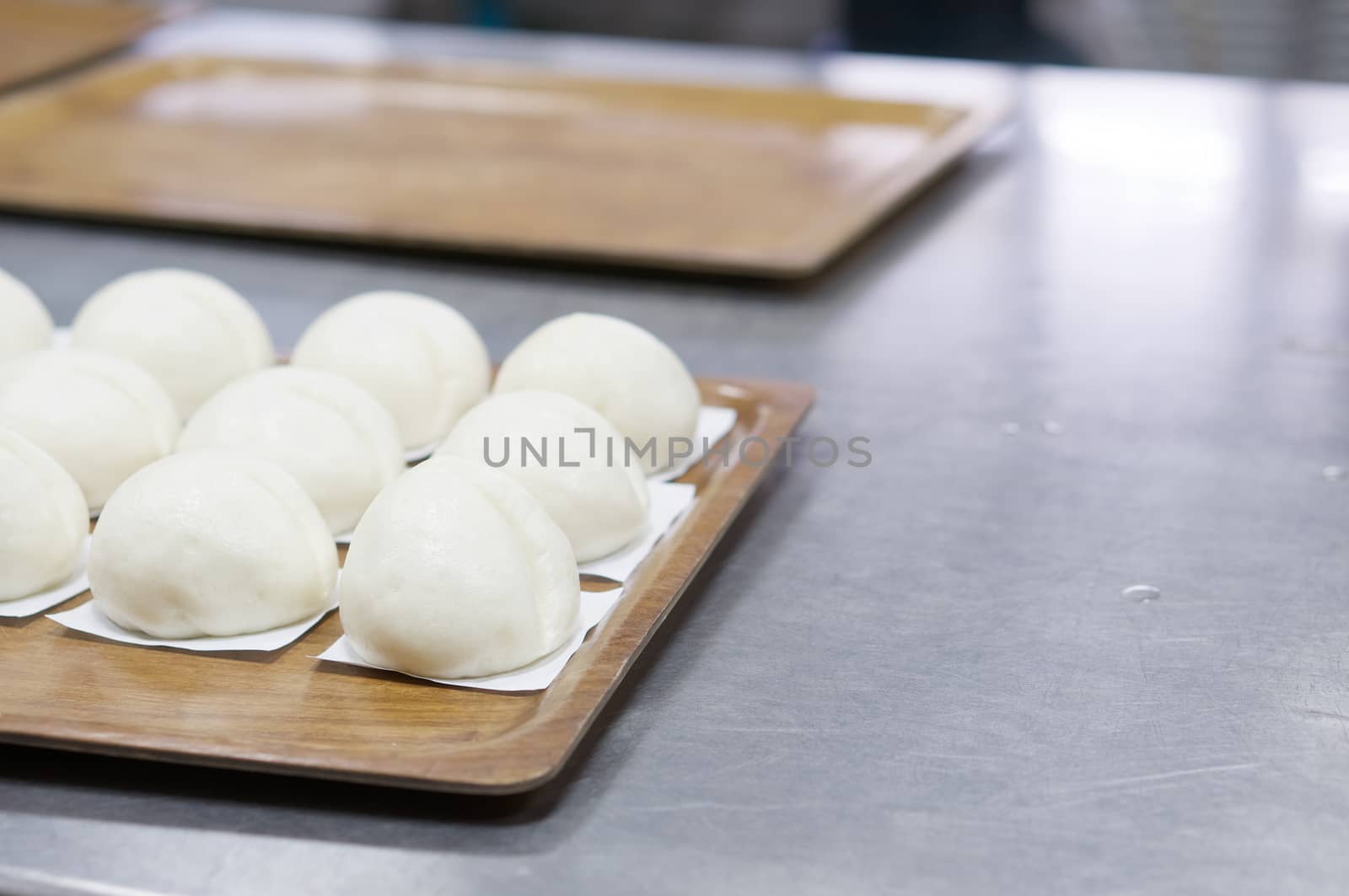 Steamed bun on white paper in brown wooden tray have aluminium table as background at restaurant kitchen with copy space. Food and healthy concept photography.