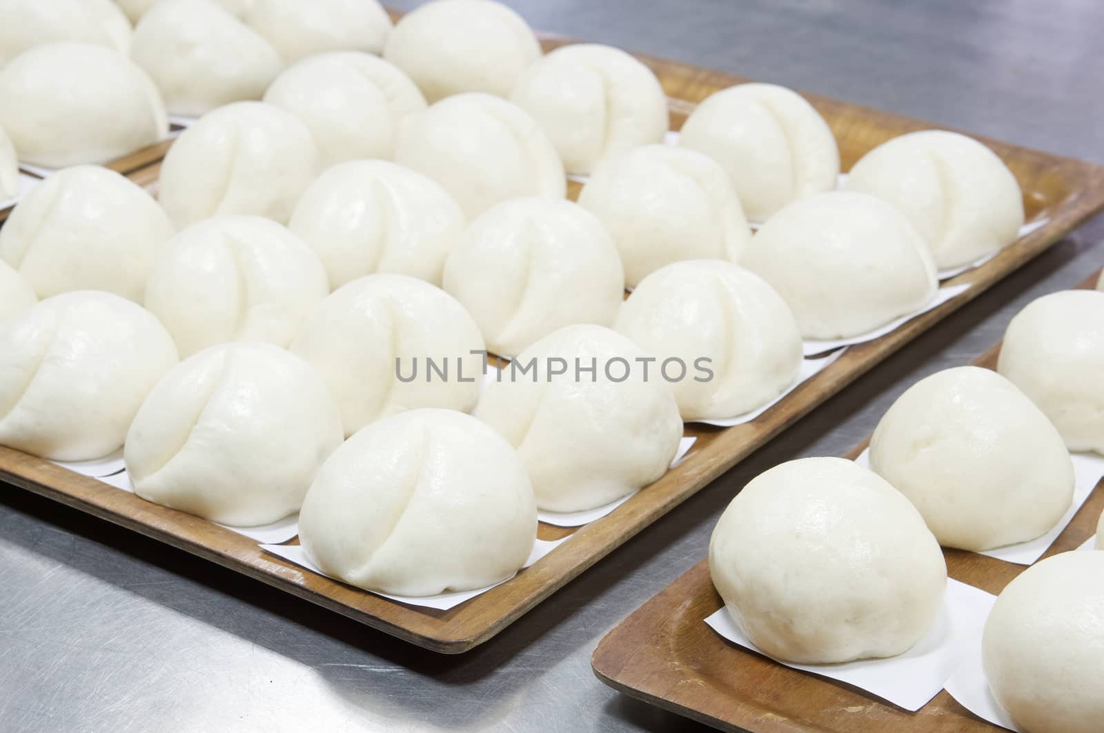 Steamed bun or dim sum on white paper in brown wooden tray have aluminium table as background at restaurant kitchen. Food and healthy concept photography.