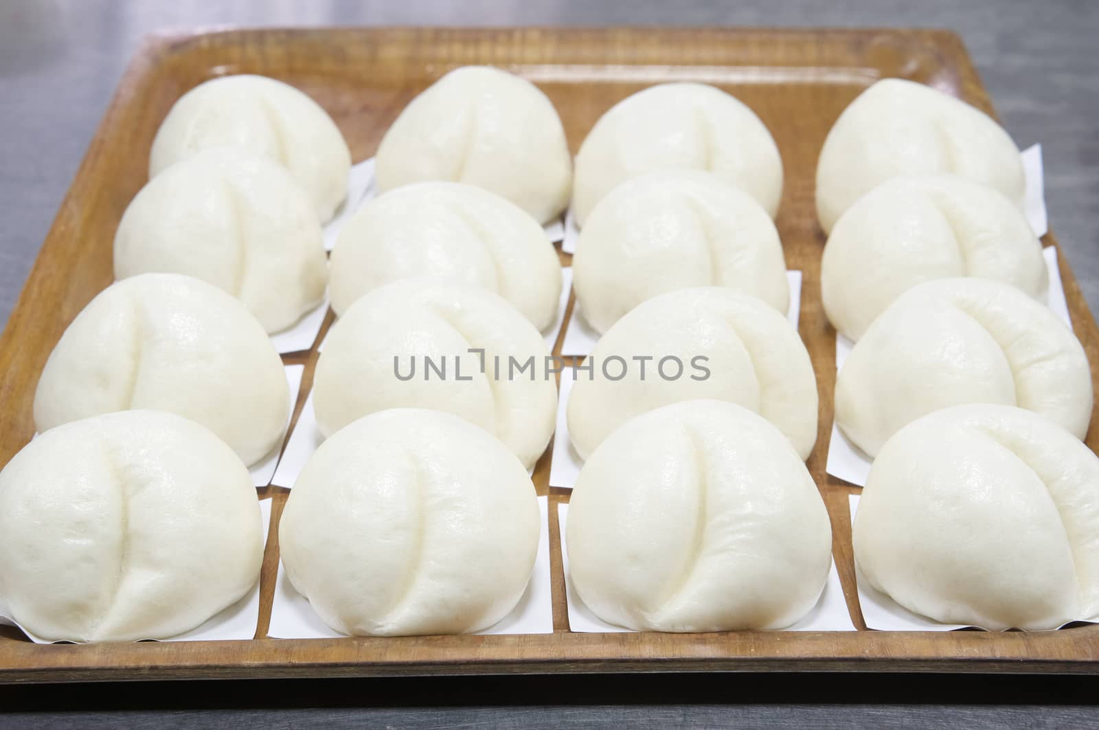 Steamed bun or dim sum on white paper put in a row in brown wooden tray have aluminium table as background at restaurant kitchen. Food and healthy concept photography.
