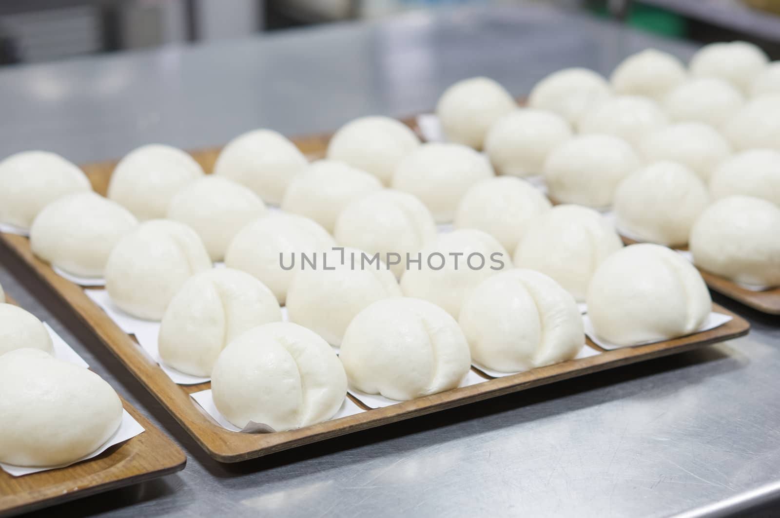 Sweet steamed bun or dim sum on white paper in brown wooden tray have aluminium table as background at restaurant kitchen with copy space. Food and healthy concept photography.