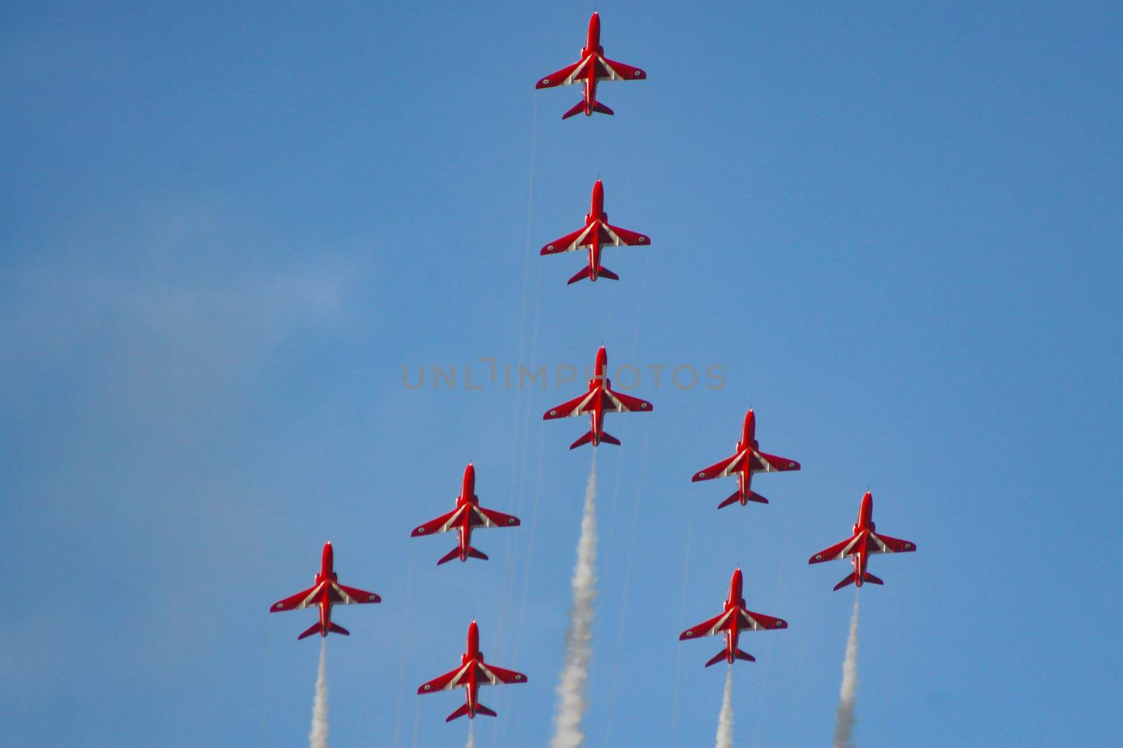 Royal air force red arrows in part of an air display flying in formation with white smoke trails in England.